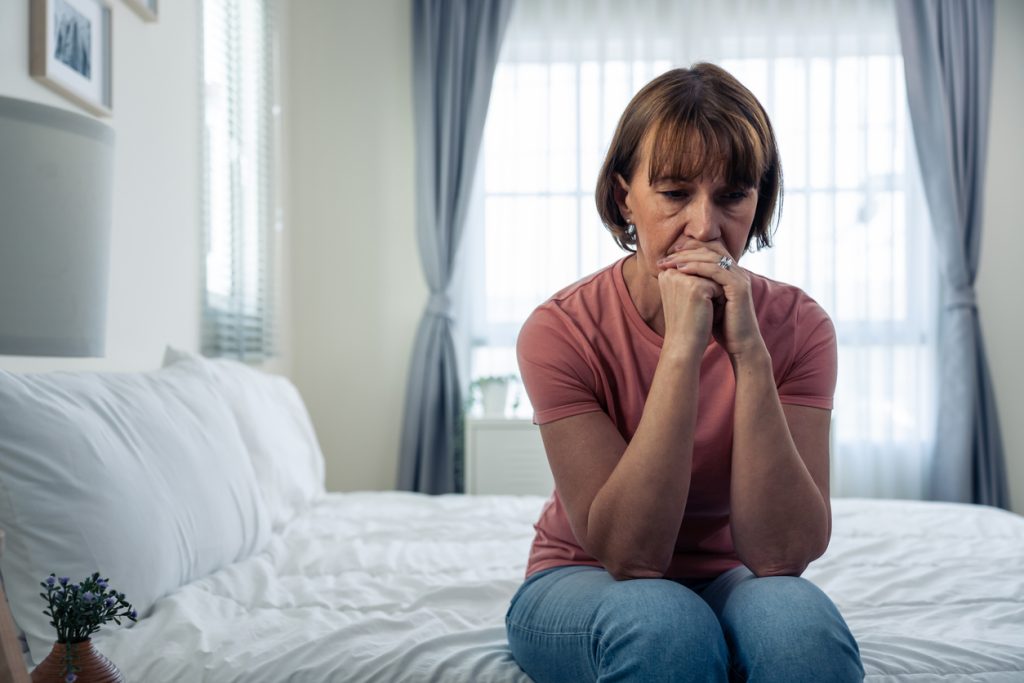 Caucasian mature woman frustrating while sit alone on bed in bedroom. Attractive old female upset depressed feel infuriating, sad and upset with life problem in house. Health care Medical Concept.